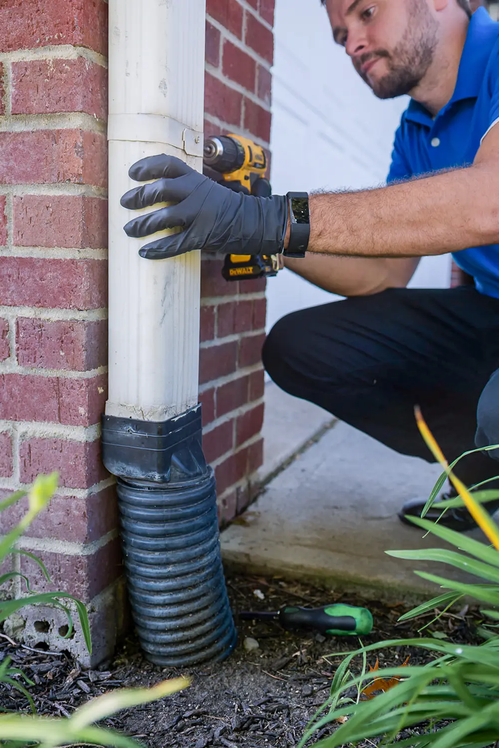 Technician kneeling to disassemble lower downspout connection